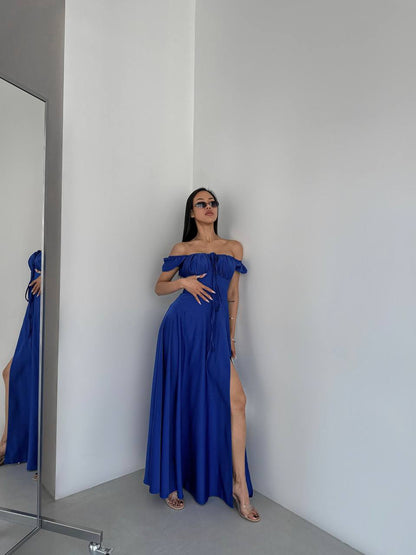 Woman in a blue off-shoulder gown standing in a minimalistic room.