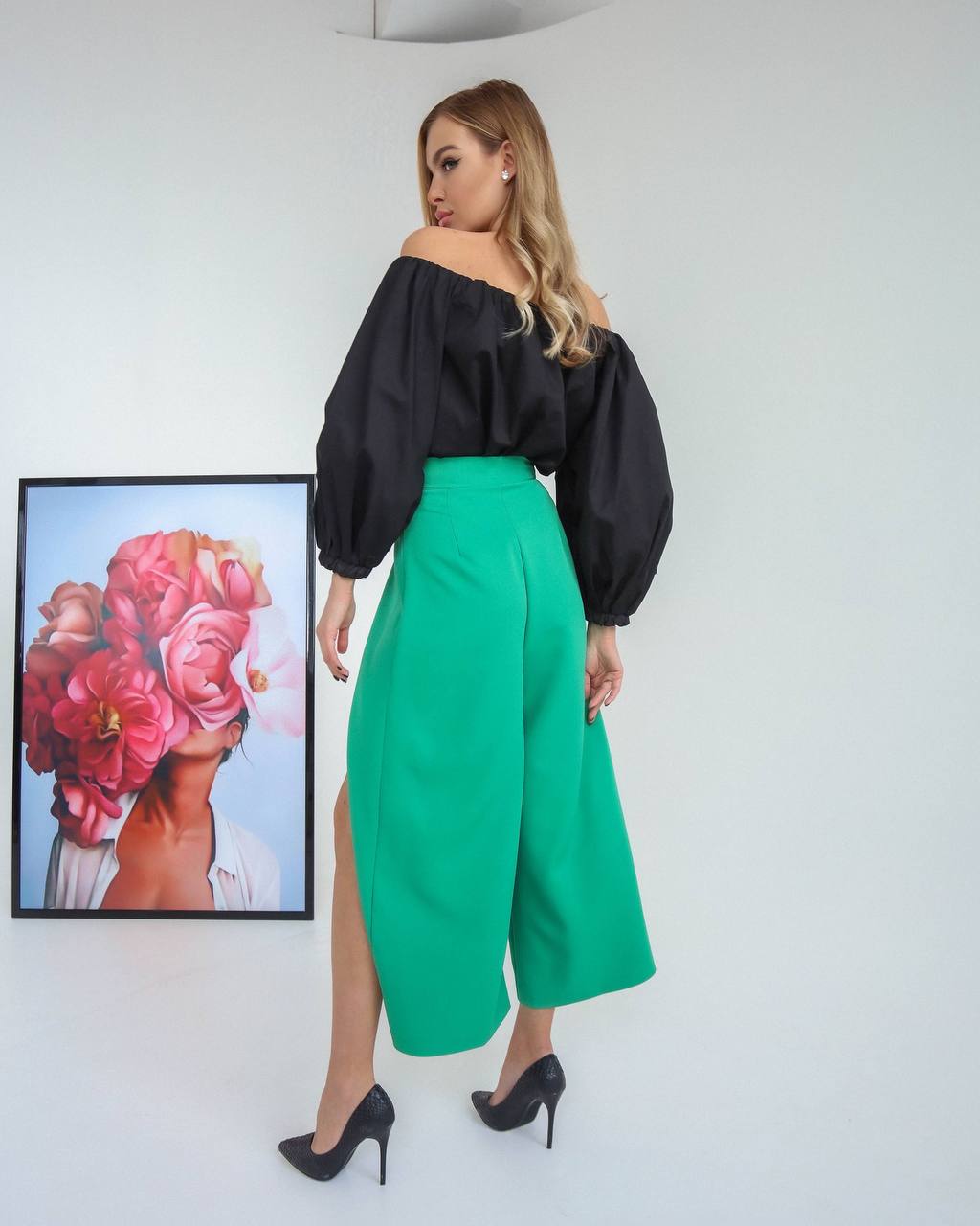 Woman wearing a black top and green skirt with a floral painting in the background