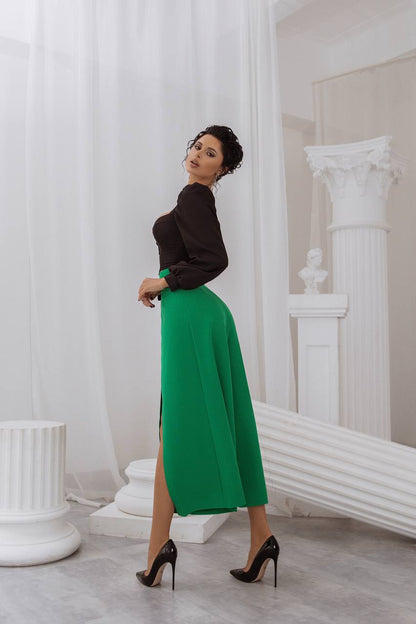Woman in a black top and green skirt standing in a classical room with white columns.