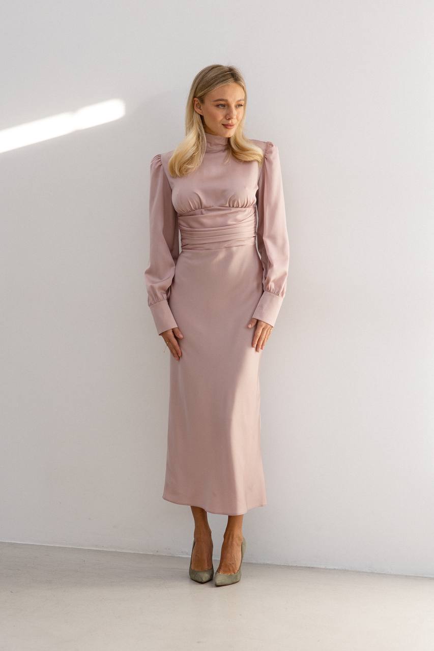 Woman wearing a pink dress standing against a white wall.