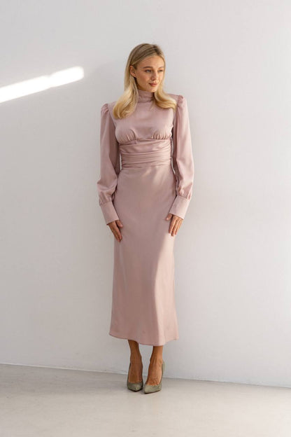 Woman wearing a pink dress standing against a white wall.