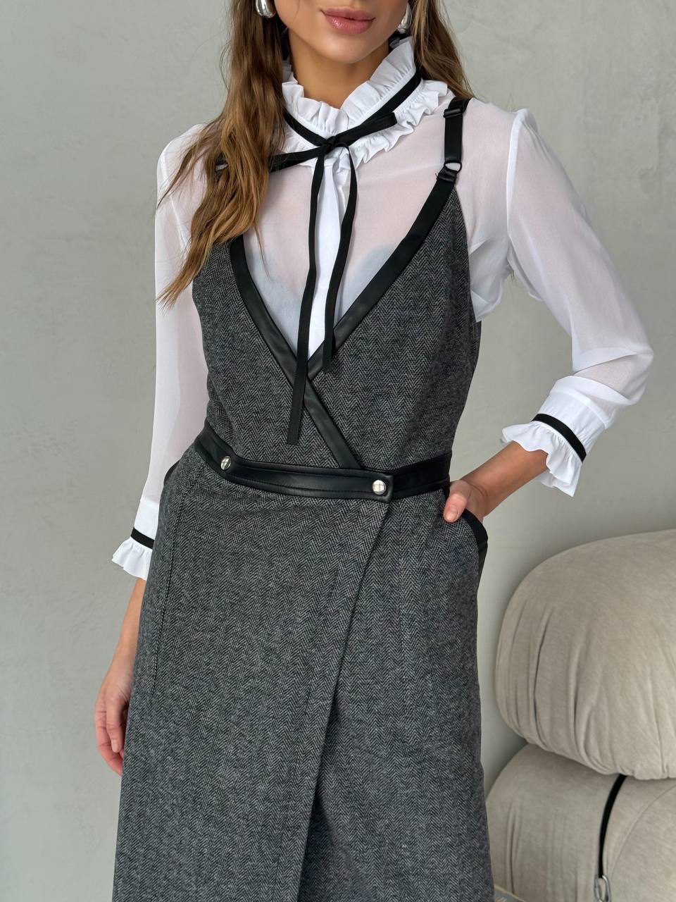 Person wearing a gray vest and pants with a white shirt and black tie against a neutral background