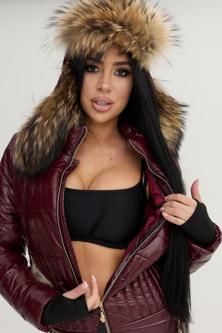 Woman wearing a maroon puffer jacket with a fur-lined hood on a white background