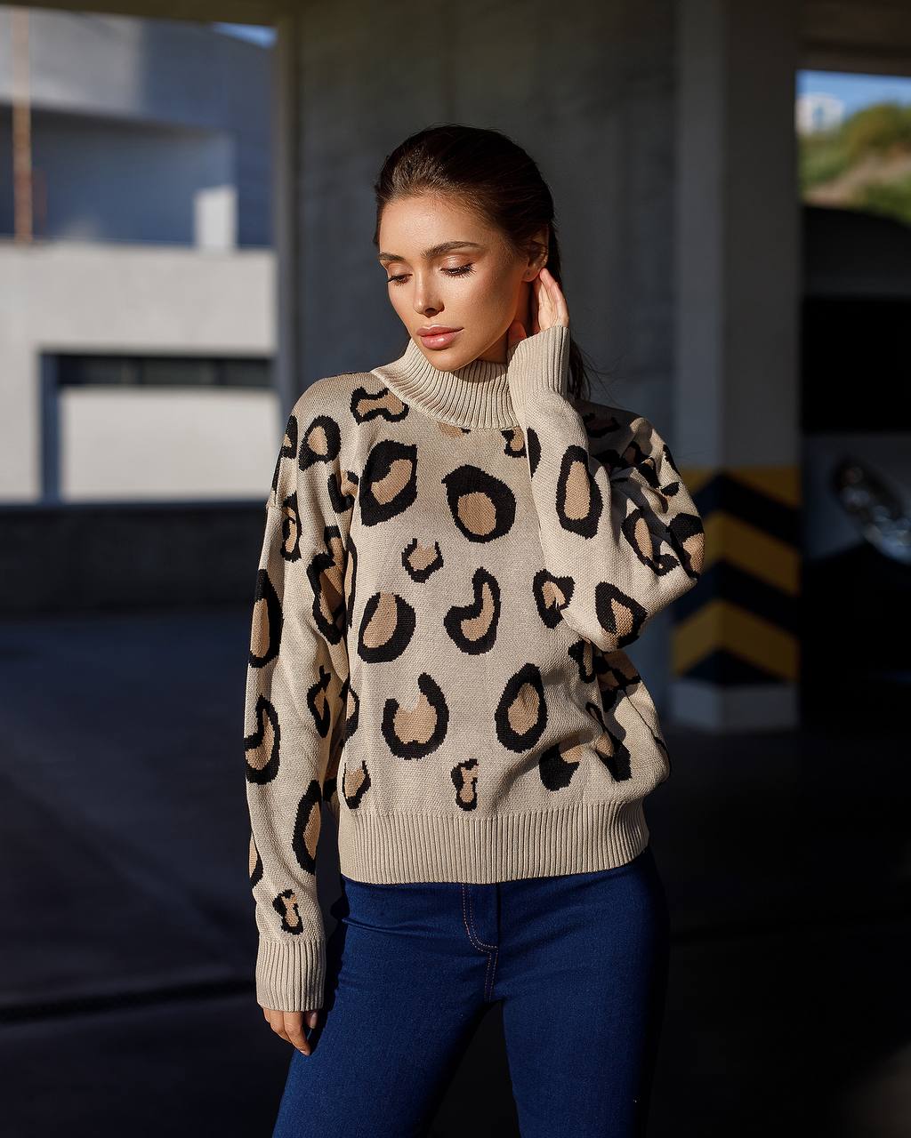 Woman wearing a beige sweater with leopard print and blue jeans in an outdoor setting