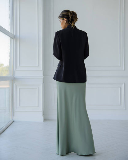 Woman wearing a black blazer and light green skirt in a bright room with white walls.