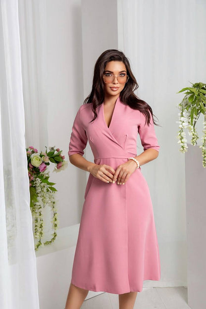 Woman wearing a pink dress standing against a white curtain background