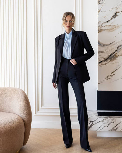 Woman in a black suit standing in a stylish room with marble wall.