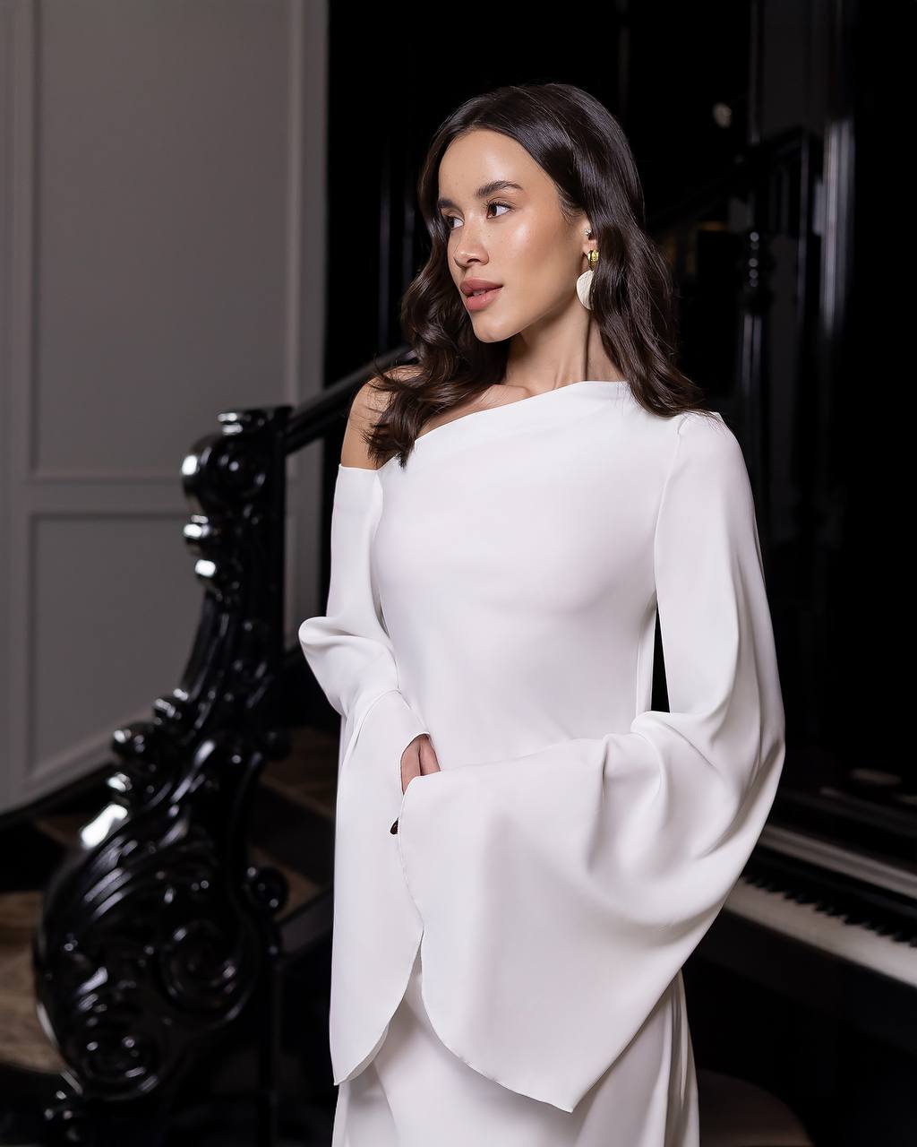 Woman in a white dress standing in a room with a piano.
