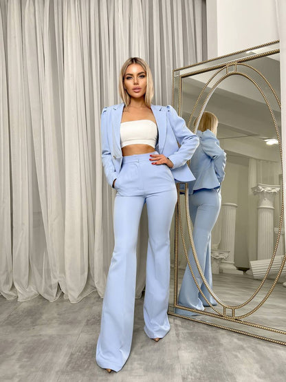 Woman in light blue outfit standing in front of a mirror in a room with curtains.