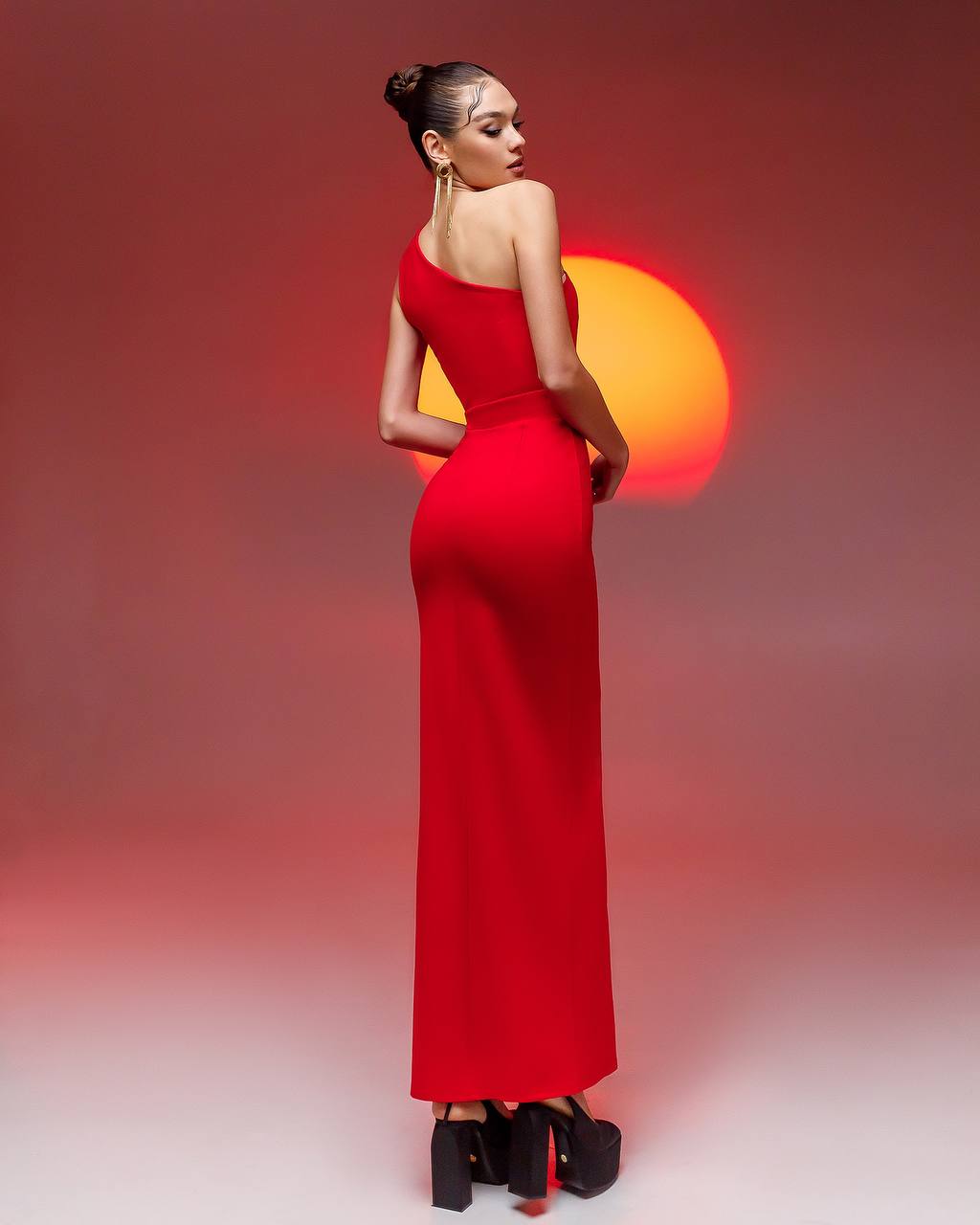 Woman in a red dress standing against a gradient background with a sun-like light source.