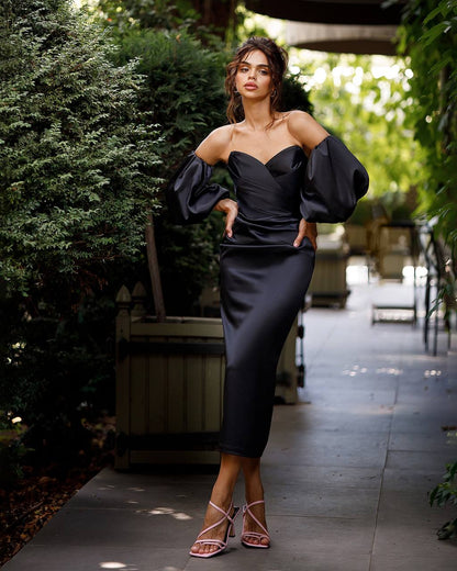 Woman in a black dress standing outdoors with greenery around