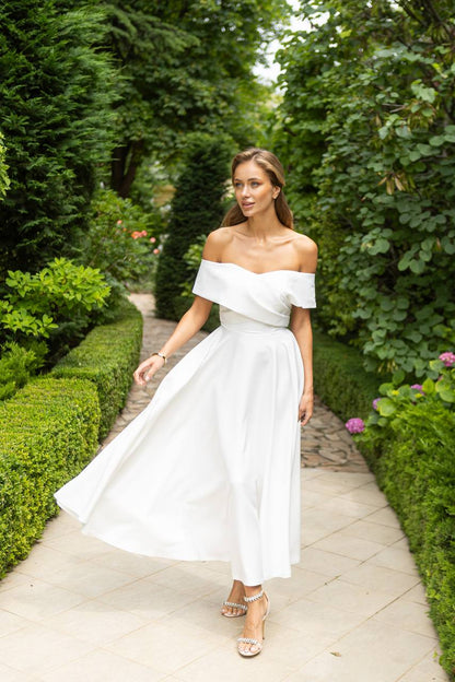 Woman in a white off-shoulder dress walking through a garden path.