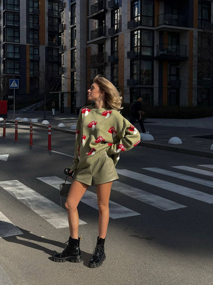 Woman in a green outfit with red patterns standing on a street corner.