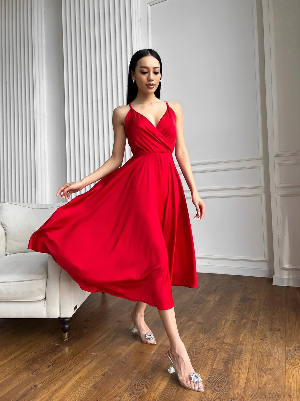 Woman in a red dress standing in a room with white walls and wooden floor.