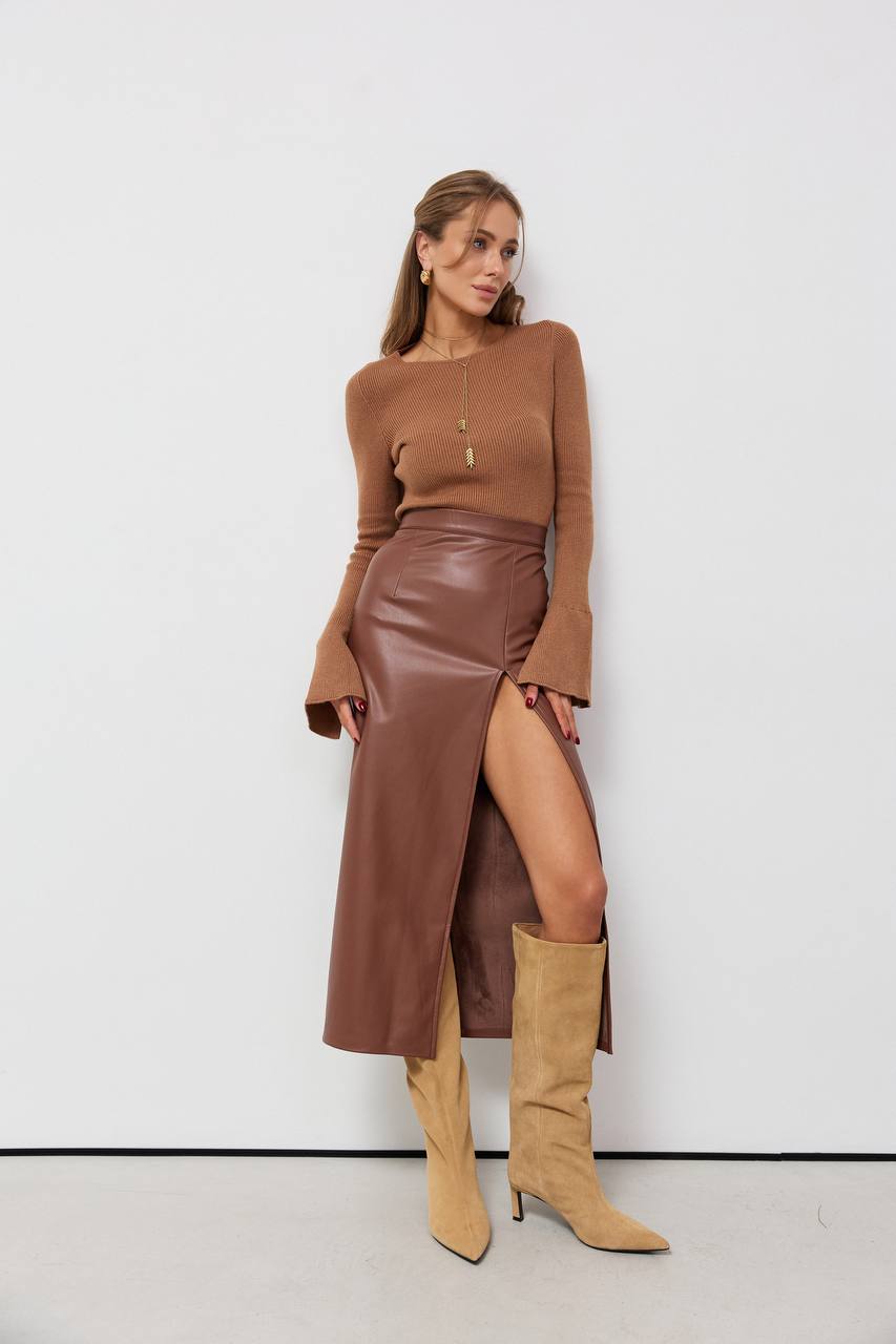Woman wearing a brown outfit with a leather skirt and knee-high boots against a white background