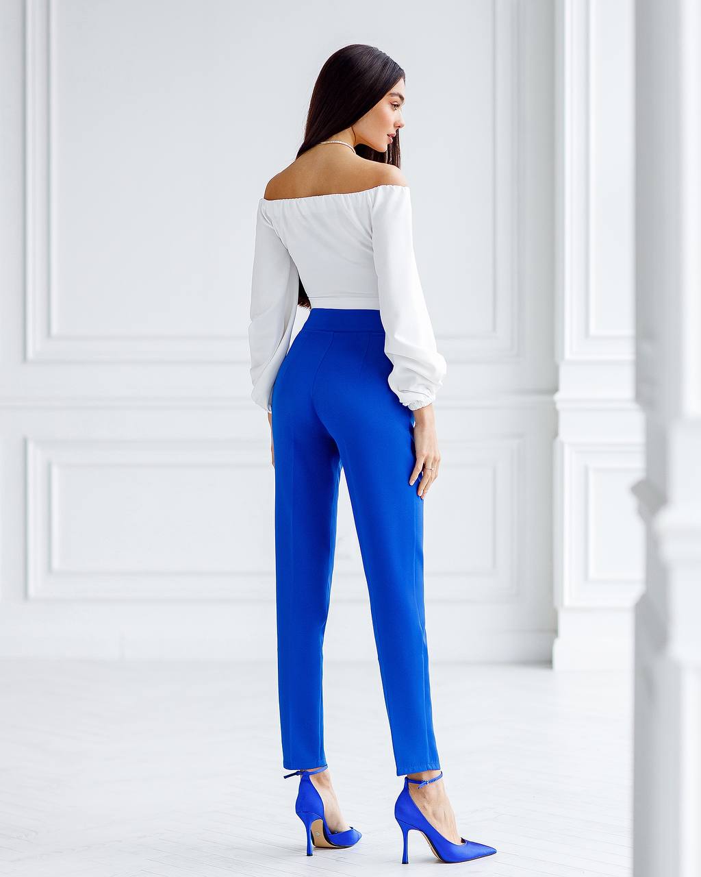 Woman wearing a white off-shoulder top and blue pants in a minimalistic setting