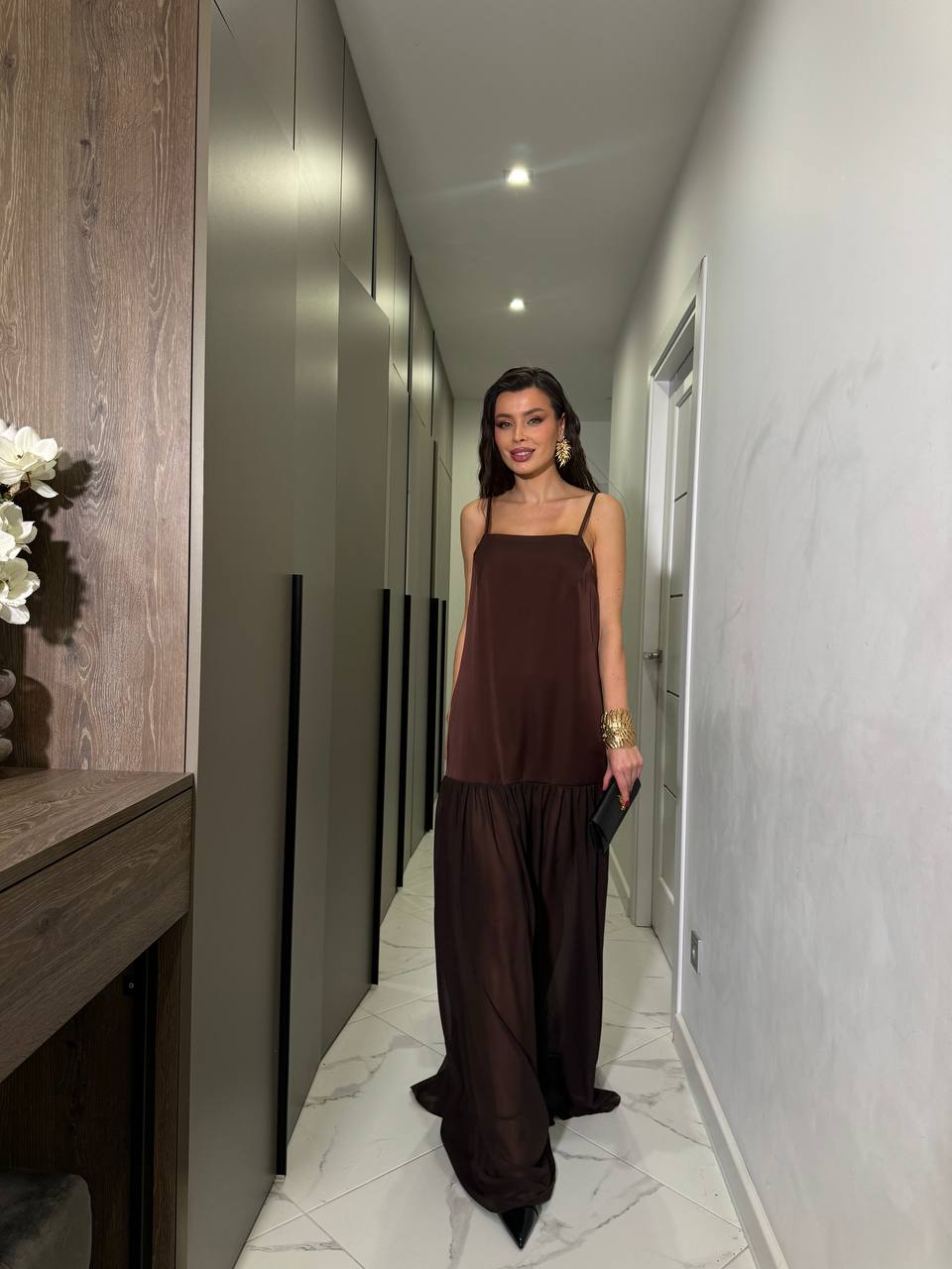 Woman in a brown dress standing in a modern hallway.