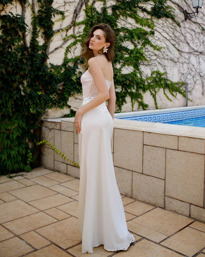 Woman in a white dress standing by a pool with greenery in the background