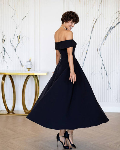 Woman in a black off-shoulder dress standing in a room with marble walls and a gold table.