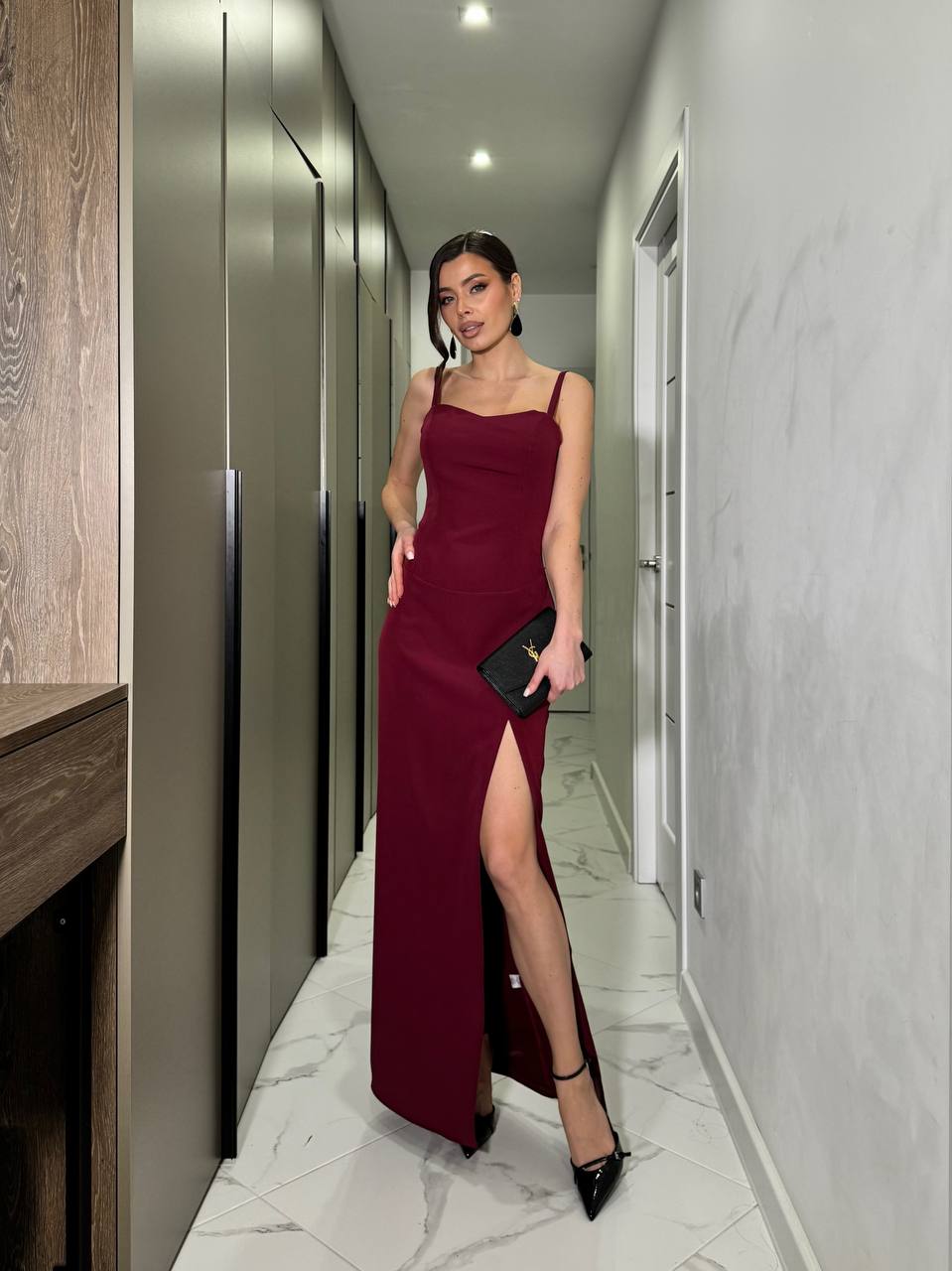 Woman in a burgundy dress with a high slit standing in a modern hallway.