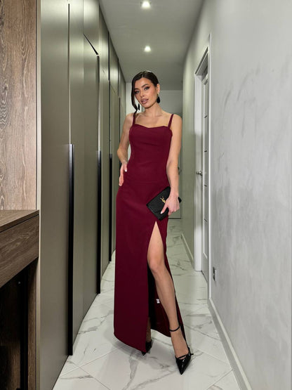 Woman in a burgundy dress with a high slit standing in a modern hallway.