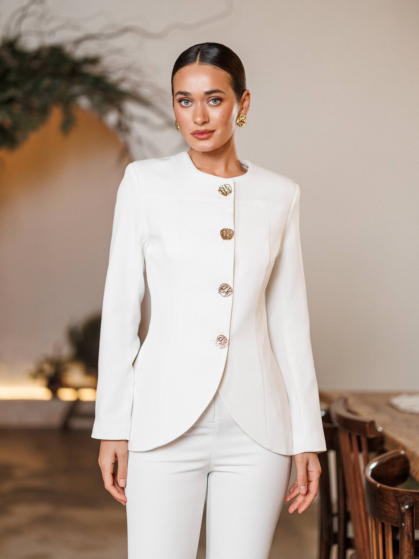Woman wearing a white suit with gold buttons in an indoor setting
