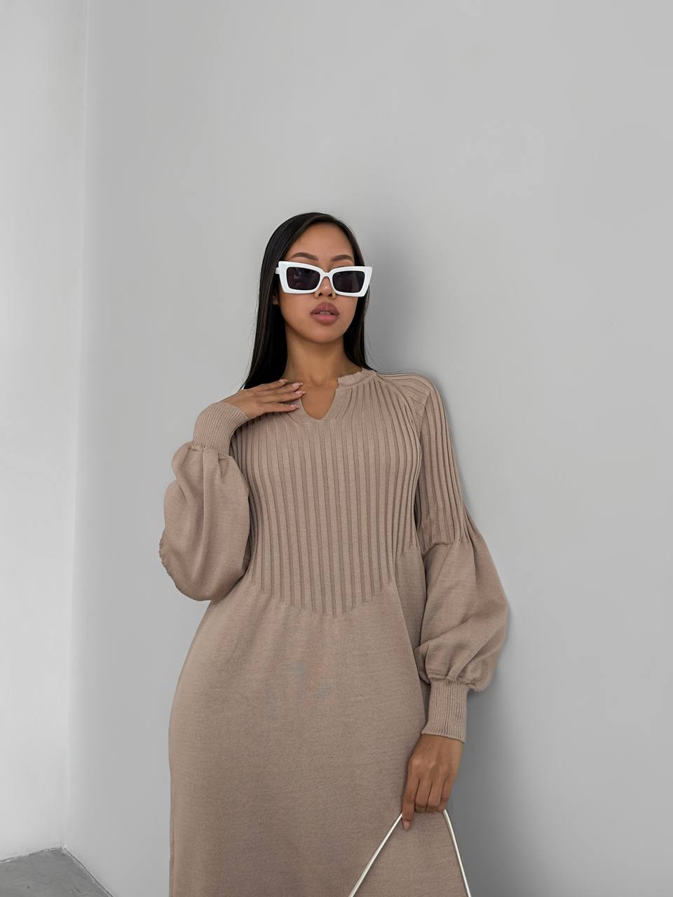 Woman wearing a beige ribbed dress and white sunglasses against a plain background