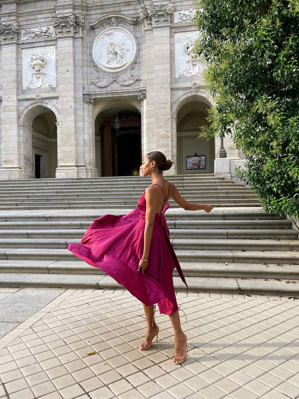 Woman in a pink dress standing on stone steps in front of an ornate building.