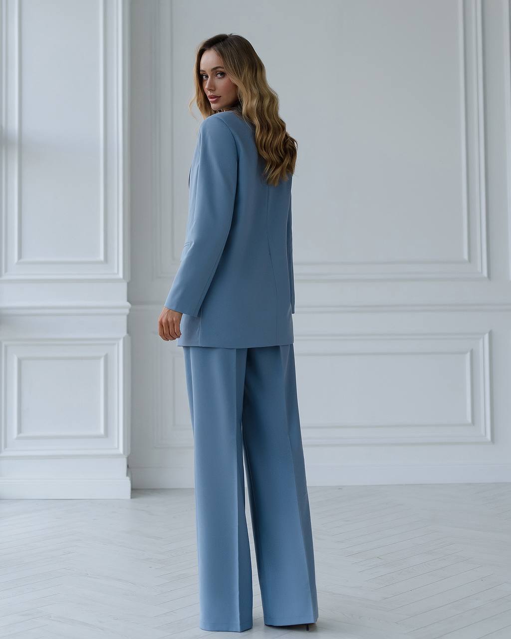 Woman wearing a blue suit standing against a white paneled wall.