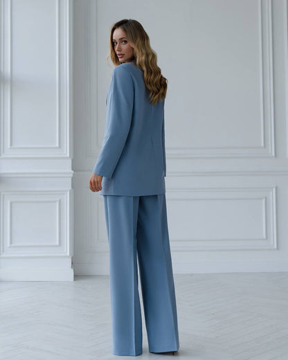 Woman wearing a blue suit standing against a white paneled wall.