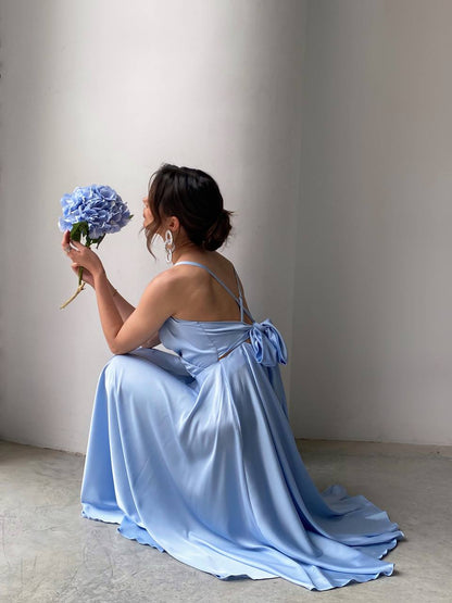 Woman in a light blue dress holding a bouquet of flowers against a plain background