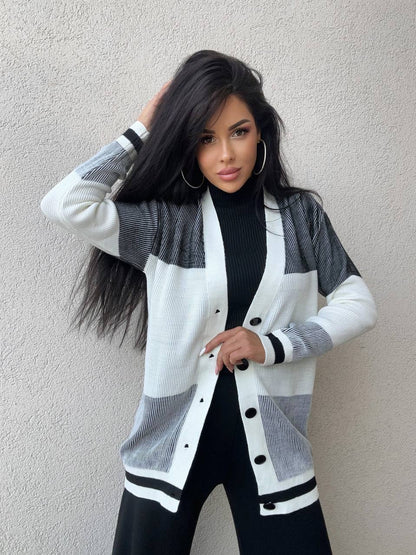 Woman wearing a white and gray cardigan over a black outfit against a plain background