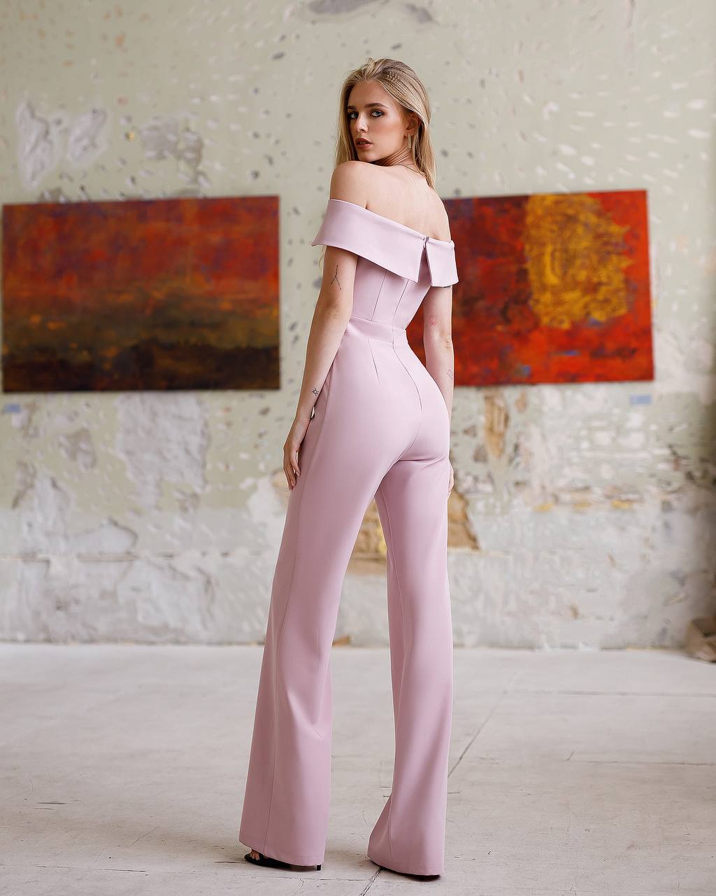 Woman wearing a pink off-shoulder jumpsuit in an art gallery setting.