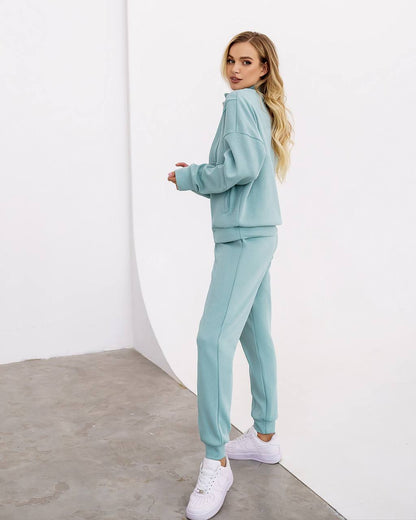 Woman wearing a light blue tracksuit with white sneakers on a white background