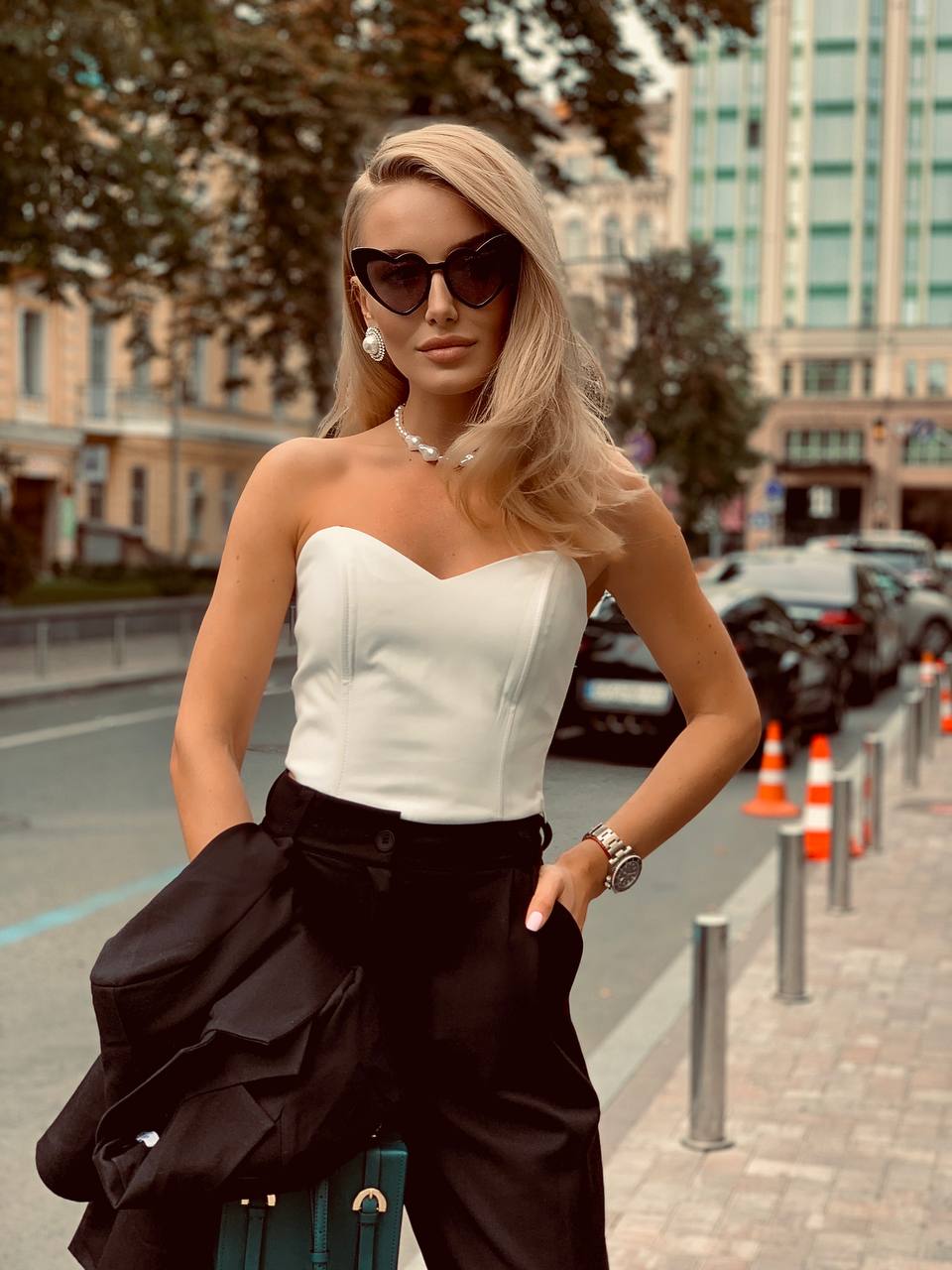 Woman in a white top and black pants standing on a city street.