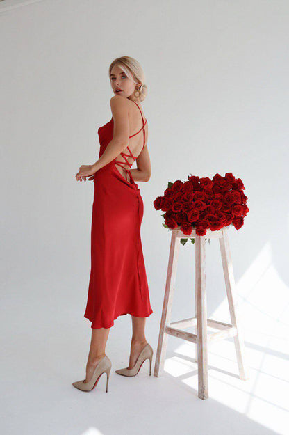 Woman in a red dress standing next to a stool with red roses on a white background