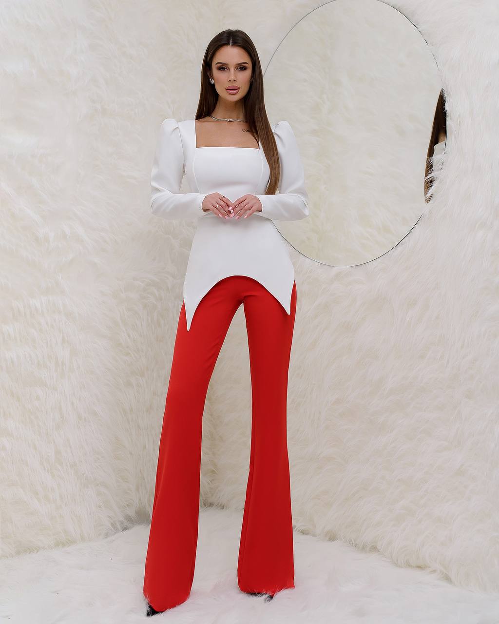Woman wearing a white top and red pants against a textured white background