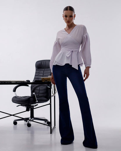 Woman wearing a light purple peplum top and dark blue jeans in an office setting.