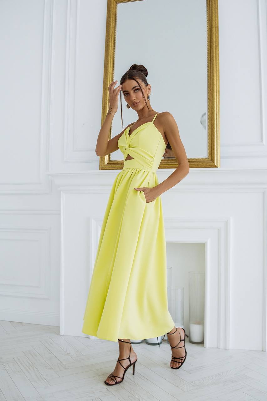 Woman in a yellow dress standing in front of a mirror in a white room.