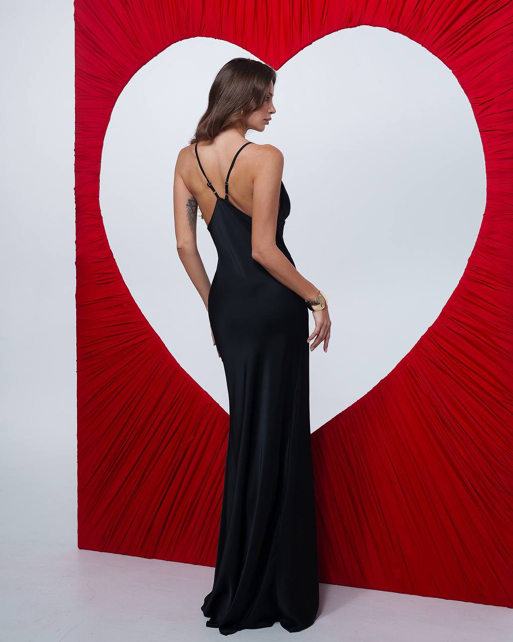 Woman in a black dress standing in front of a red heart-shaped backdrop