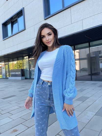 Woman wearing a light blue cardigan, white top, and jeans standing outside a building.