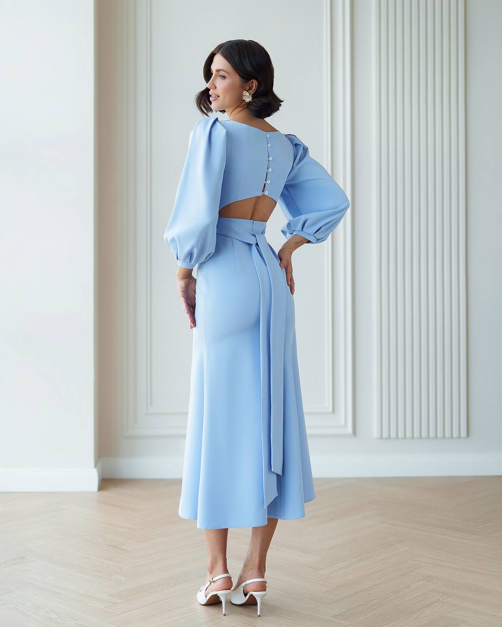Woman wearing a light blue outfit with a matching top and skirt in a minimalistic room.