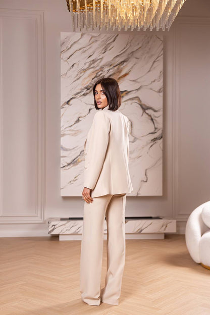 Woman in a beige suit standing in a stylish room with marble wall art and modern decor.