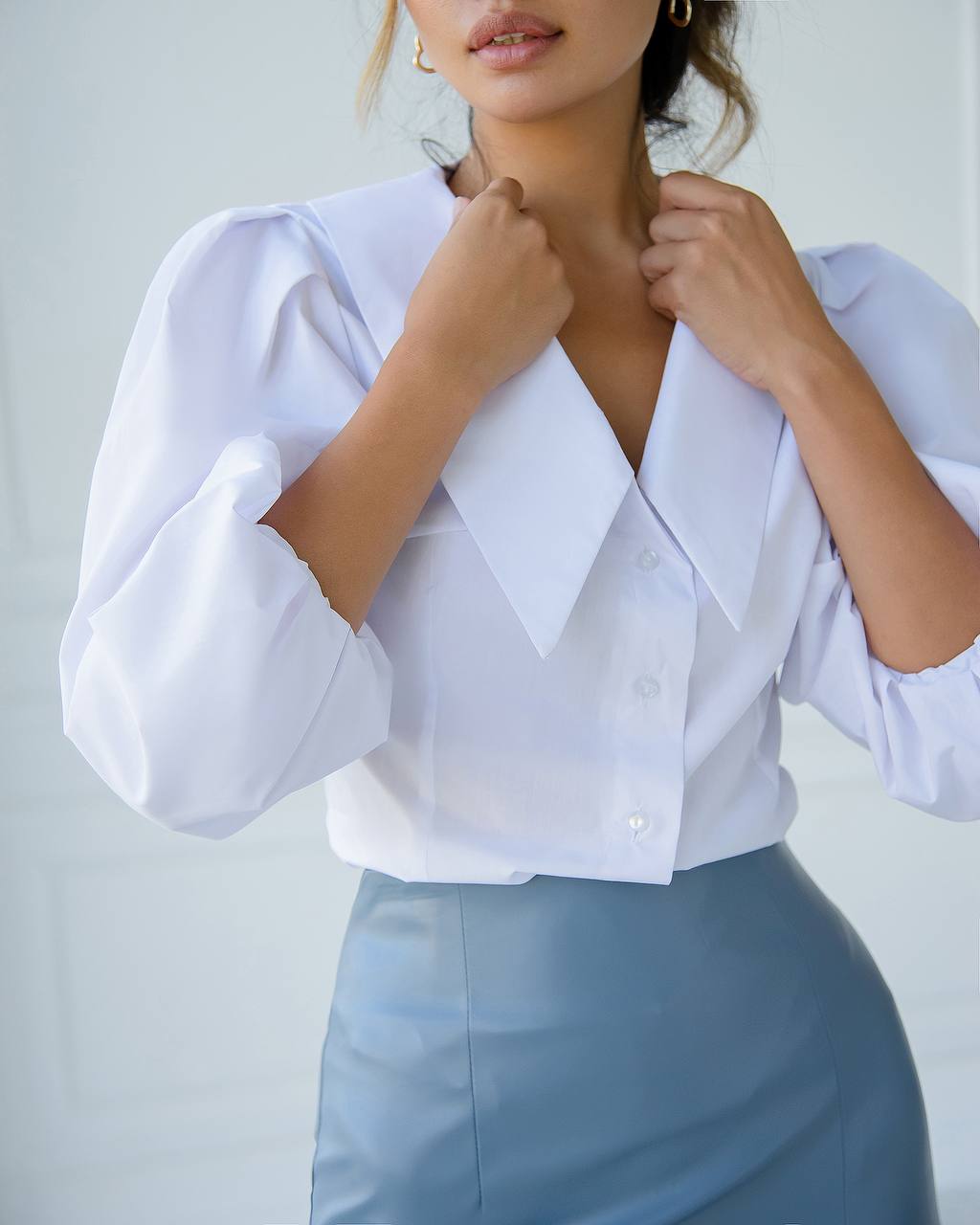 Woman wearing a white blouse with puffed sleeves and a blue skirt against a light background