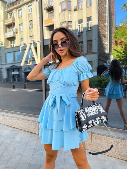 Woman in a light blue dress holding a black and white handbag on a city street.