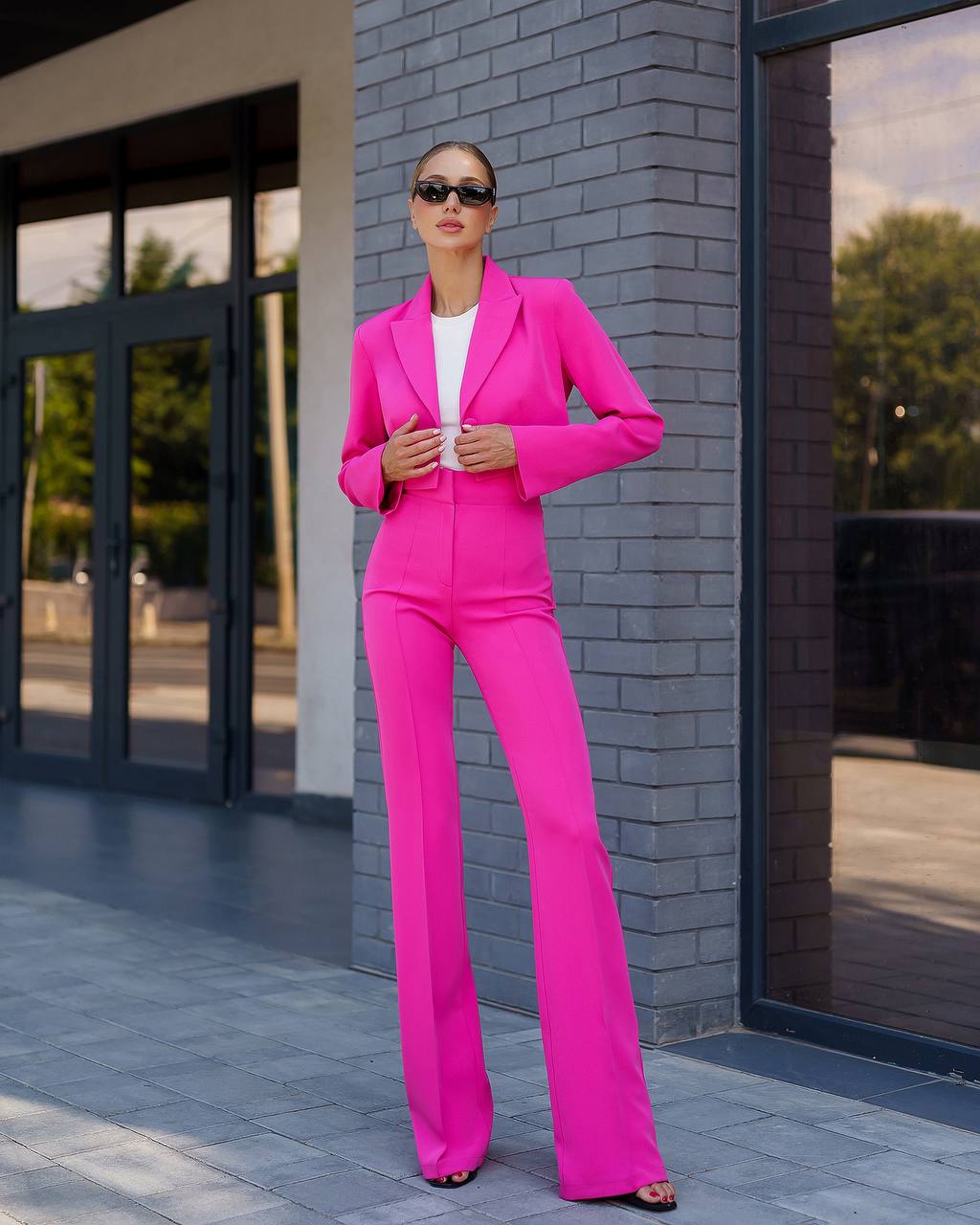 Woman in a bright pink suit standing against a brick wall.