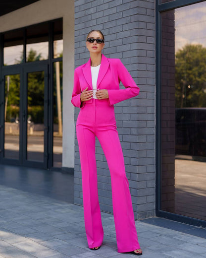 Woman in a bright pink suit standing against a brick wall.