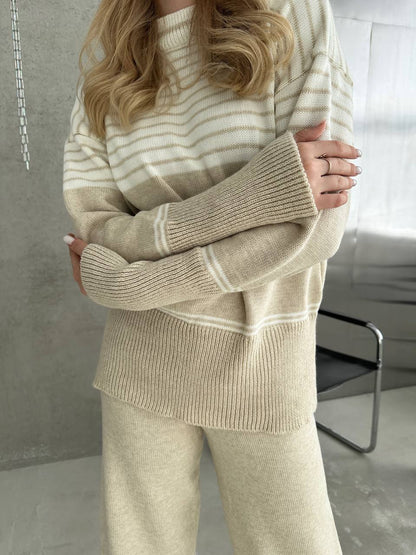 Person wearing a beige and white striped sweater and pants in a minimalistic room.