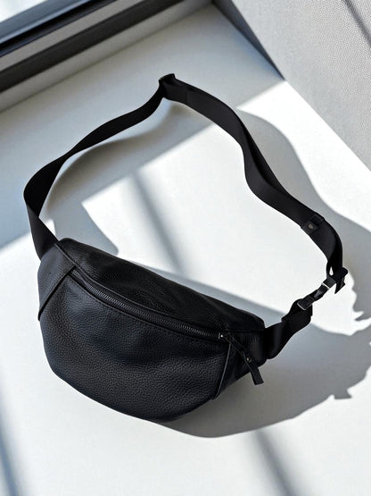 A black pebbled leather fanny pack with an adjustable strap, photographed on a white surface with strong diagonal shadows.