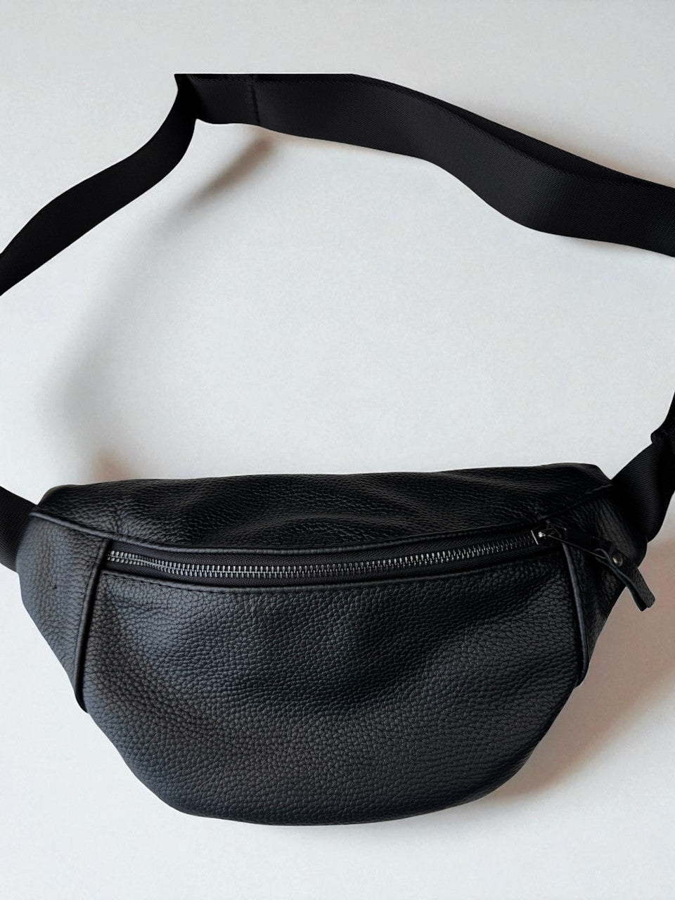 A black pebbled leather fanny pack with a matching adjustable black strap, shown against a plain light gray background.